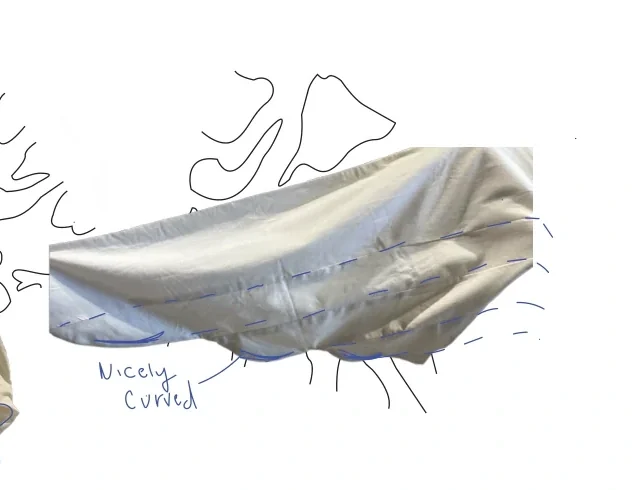 Close view of a pale Fantasy Dress toile sleeve draped into a long sculptural curve with blue fitting annotations.